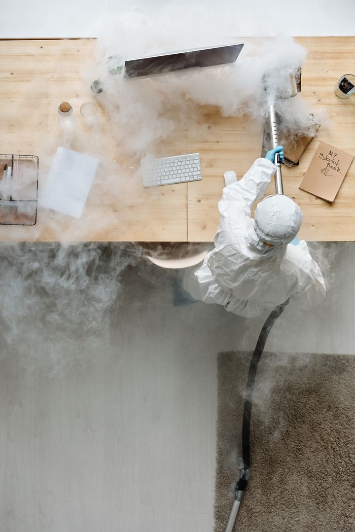 our-story A person in protective gear sanitizing an office desk using fumigation equipment during daytime.