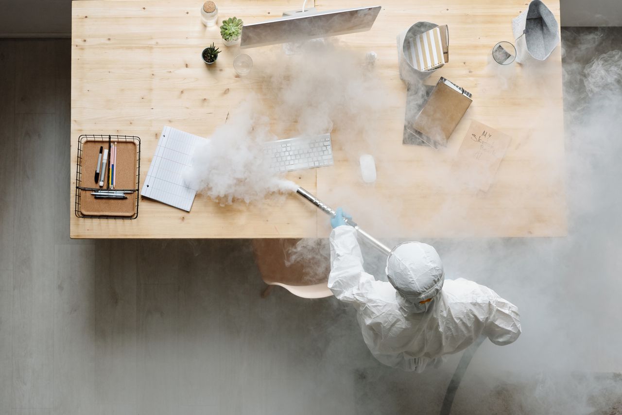 home-img An individual disinfects a workspace using fumigation, wearing full protective gear for safety.